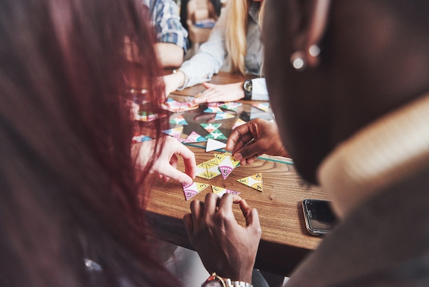 Gruppo di amici multietnici creativi che si siedono al tavolo di legno. persone che si divertono mentre giocano a giochi da tavolo