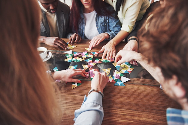 Group of creative multietnic friends sitting at wooden table. People having fun while playing board game