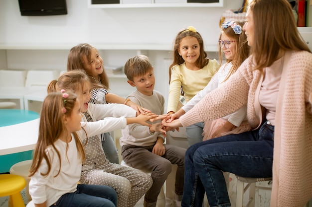 Group of cute preschool kids put hands together with their nursery teacher