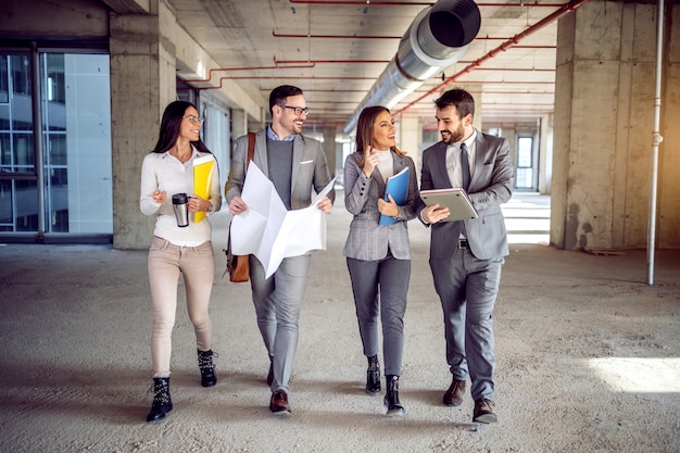 Group of dedicated highly motivated architects walking in building in construction process and talking about ideas how to renew an old building into modern business center.