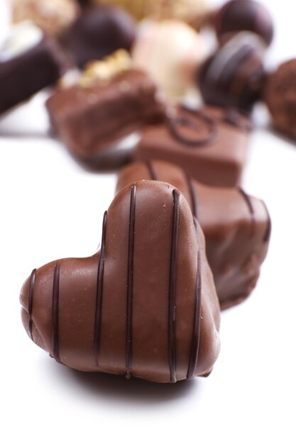 Group of delicious candies with chocolate heart in the foreground on white background