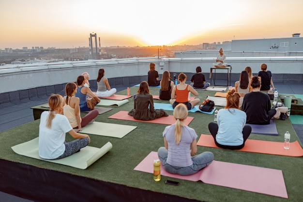 Gruppo di persone diverse stanno facendo pratiche di yoga meditativo sul tetto su un bel tramonto in una sera d'estate