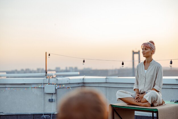 Group of different people are doing meditative yoga practices at the rooftop on a beautiful sunset at summer evening