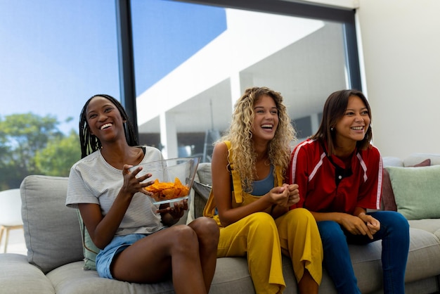 Group of diverse happy female friends sitting on sofa, watching sport on tv