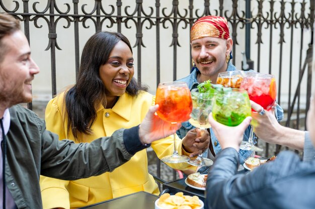 Foto gruppo di persone diverse che brindano drink al cocktail bar, amici che si divertono durante l'incontro, focus sulla donna afroamericana, persone che bevono mojito, spritz e mocktail