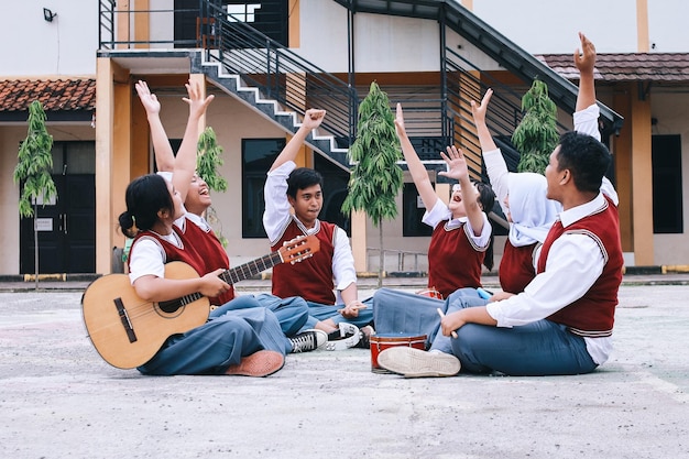 group of diverse students sitting in circle and raising hands before practicing music performances