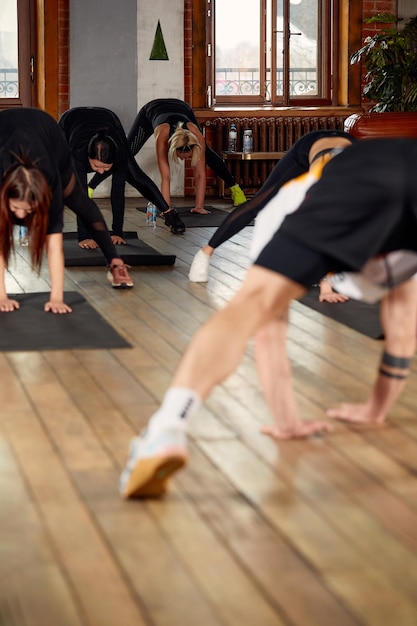 Group of diverse young people in sportswear doing stretching exercises together at the gym