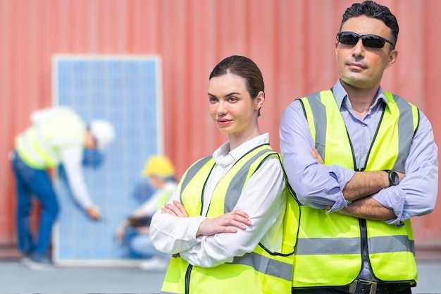 Группа людей рабочего завода разнообразия мужчина и женщина, стоящие перед логистическими контейнерами на складе. Штабы рабочих проверяют панель солнечных батарей для строительства возобновляемых источников энергии.