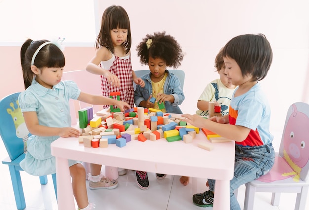 Группа разнообразных детей, играющих с разноцветными блоками на столе в классе в детском саду Концепция международного школьного образования