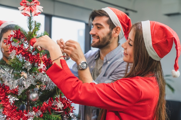 Group of diversity young creative happy celebrating Merry Christmas and Happy New Year decorating Christmas tree in office in modern office