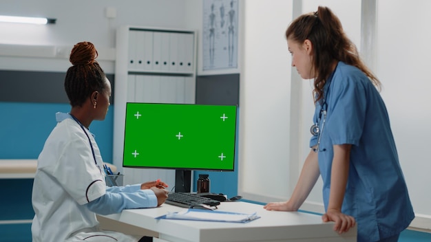 Photo group of doctor and nurse working with green screen on monitor in doctors office. medical team looking at computer with chroma key and mockup isolated template or background on display.