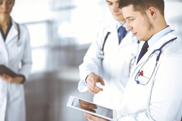 Group of doctors are checking medical names on a computer\
tablet, with a nurse with a clipboard on the background, standing\
together in a hospital office. physicians ready to examine and help\
patients