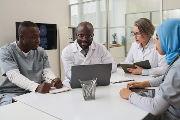 Group of doctors examining xray image on laptop together and discussing it during meeting in office