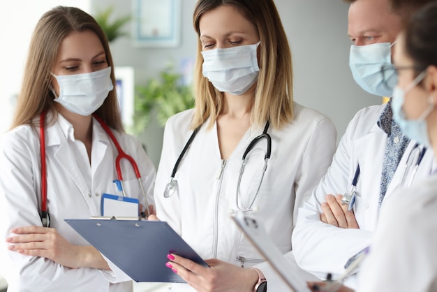 group of doctors in medical protective masks standing with clipboards with documents in clinic