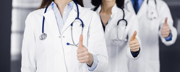 Group of doctors standing as a team with thumbs up in sunny clinic. Good news and Hope for a cure. Medicine concept during Coronavirus pandemic. Covid-2019.