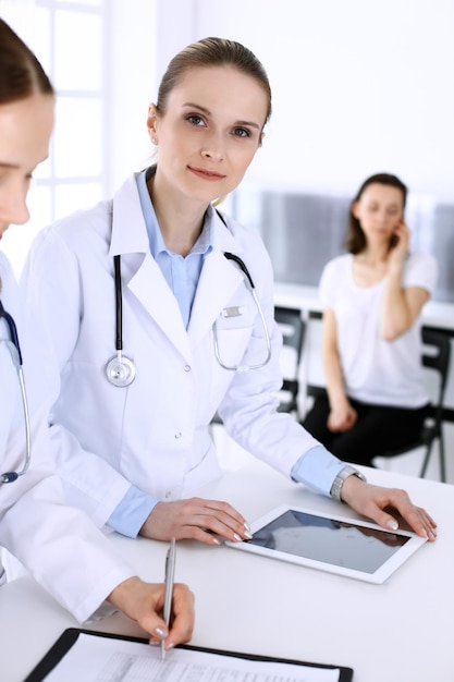 Group of doctors at work in hospital with patient in a queue at the background