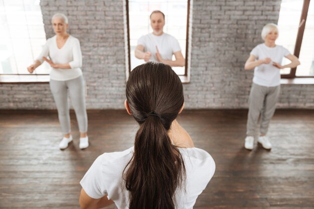 Group of elderly people wearing cozy clothes looking at their instructor while doing yoga exercises