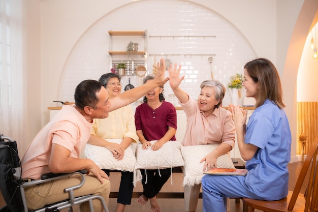 Photo group of elderly and senior man in wheelchair with nurse at nursing home play a fun game of hitting each other's hands elderly people in nursing home concept