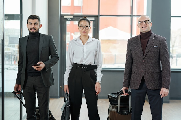 Gruppo di eleganti viaggiatori d'affari di varie etnie ed età in piedi in aeroporto prima della partenza