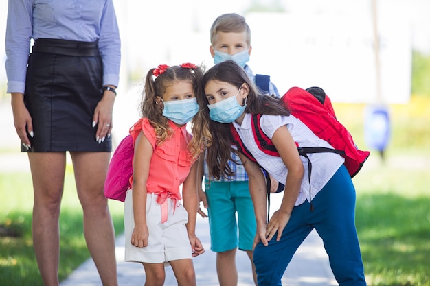 Photo group of elementary schoolchildren in facial protective masks posing together outdors near their teacher education healthcare and pandemic concept