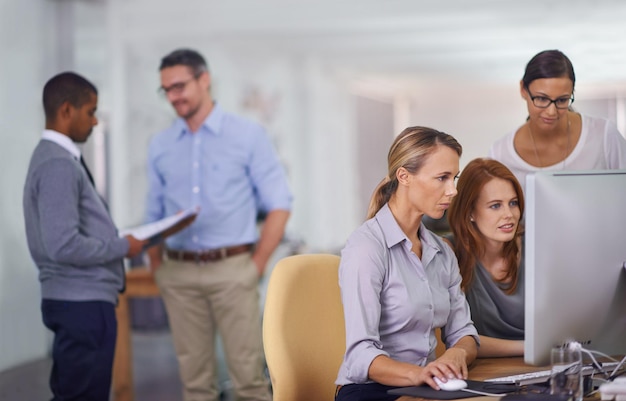 Group of employees at work talking collaborating and brainstorming on a computer Diverse team working together on a project in the office Marketing agency with busy colleagues browsing technology