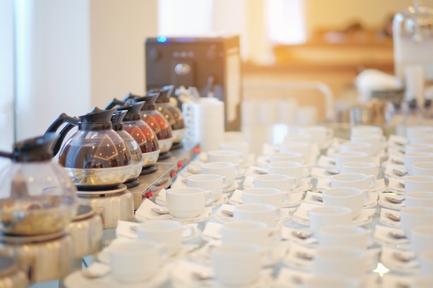 Group of empty Many rows of white ceramic coffee or tea cups and spoons on glass table