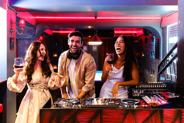 Group of energetic women dancing friends with DJ enjoying night party Young women dance and hold a w