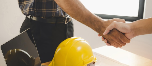 Group of engineer architect construction worker team hands\
shaking after plan project contract on desk in meeting room office\
at construction site contractor partnership construction\
concept