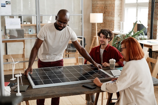 Группа инженеров, работающих за столом в команде, они разрабатывают новую солнечную батарею в офисе
