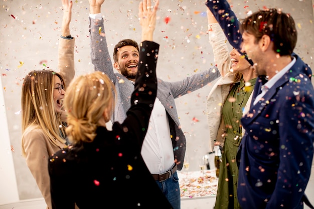 Group of excited business people celebrating and toasting with confetti falling in the office