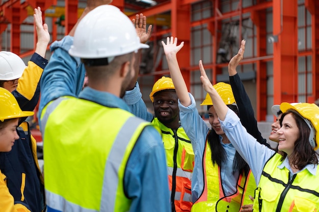 Группа фабричных рабочих в касках с поднятыми руками празднует успех