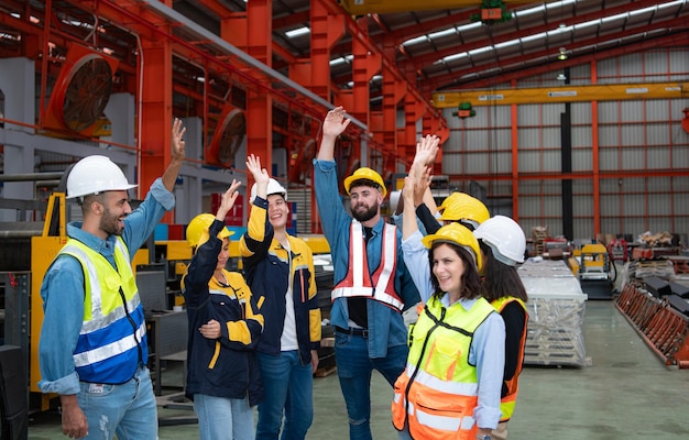 Group of factory workers in hardhats with arms raised celebrating success