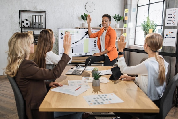 group of female financiers holding one hand up while voting at office room