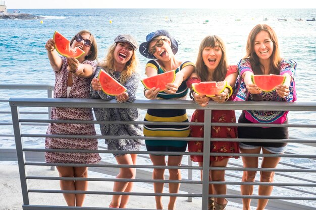 Group of female friends holding watermelon while standing on bridge