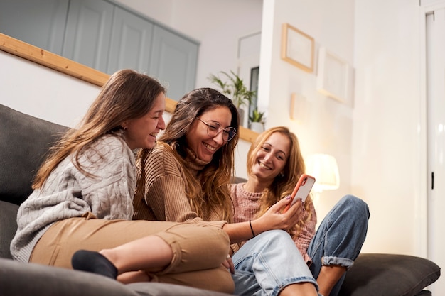 Group of female friends on the sofa at home, using a mobile phone laughing