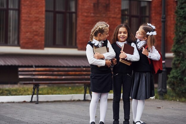 Photo group of female kids in school uniform that is outdoors together near education building.