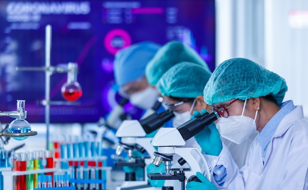 Group of female researchers or scientists wearing protective hygiene masks and medical uniforms working with microscopes in laboratory studying and analyzing about coronavirus situation