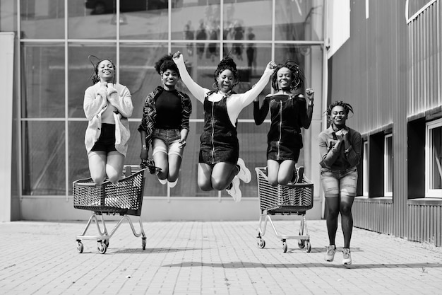 Group of five african american woman with shopping carts having fun together and jumping outdoor