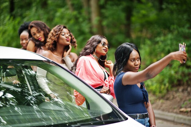 Group of five happy traveler women making selfie against car