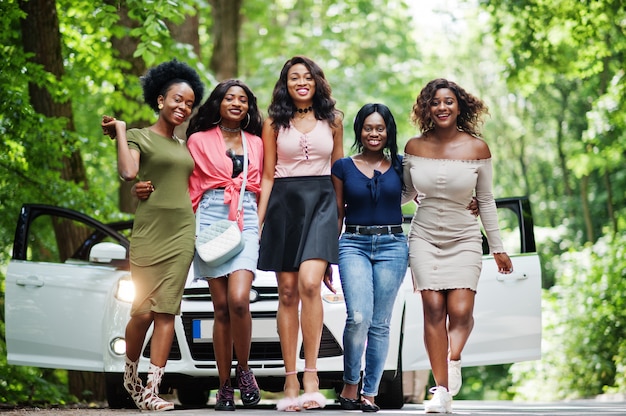 Group of five happy walking against white car