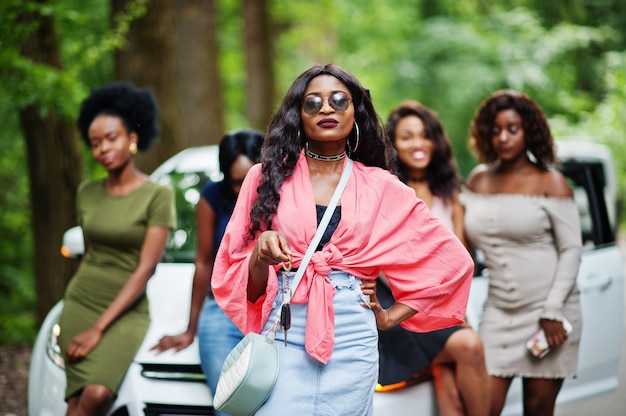 Group of five happy women posed against car, one of them show keys