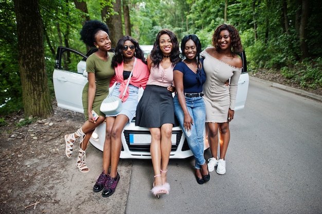 Group of five happy women sitting on a car hood