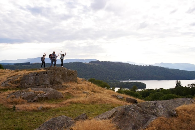 A group of five happy young adult friends cheer with their arms in the air at the summit after a mountain hike