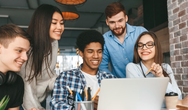 a group of five multiethnic students is gathered around a laptop engaged in a collaborative effort
