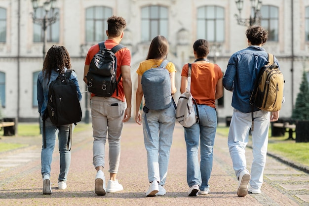 バックパックを持った5人の学生のグループが大学キャンパスで一緒に歩いています