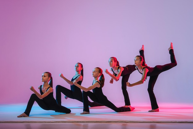 Group of five teenagers balrins in black tightfitting costumes are dancing modern konteporari on a l