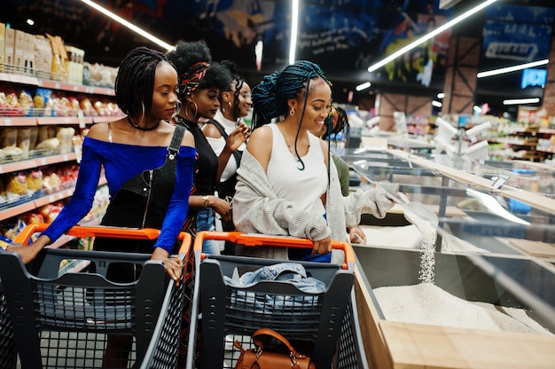 Group of five women with shopping carts choose rice and other groats in supermarket