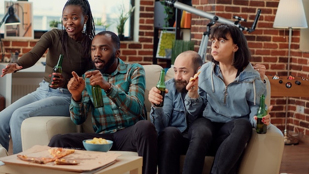 Group of football fans watching championship match on\
television, cheering to win game and tournament. drinking beer and\
showing support while they watch sport competition. handheld\
shot.