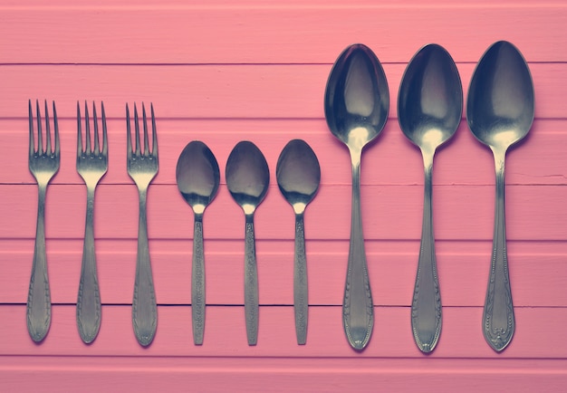 A group of forks, a spoons on a pink wooden table