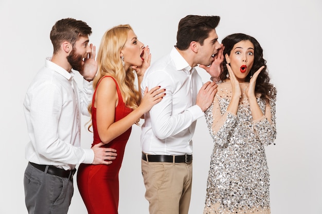 Group of four cheerful people smart dressed telling secrets to each other isolated over white